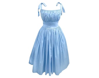 Puede incluir: Un vestido azul claro sin mangas con un corpiño fruncido y una falda completa. El vestido tiene tirantes finos que se atan en los hombros.