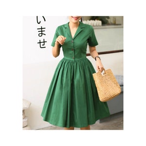 May include: A solid green midi dress featuring a notched lapel collar, short sleeves, and a button-down front closure. The bodice is fitted, transitioning into a full, pleated skirt that falls below the knee. A woven straw handbag is held at the side.