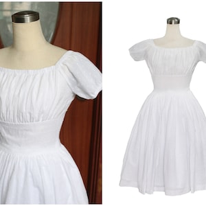 May include: A white cotton dress with a square neckline, short puff sleeves, and a fitted bodice. The skirt is full and gathered at the waist.