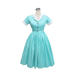 May include: A light turquoise dress featuring a white notched collar and white sleeve cuffs. The dress has short sleeves, a button-down front with three visible brown buttons, and a full, pleated skirt that falls to the knee.