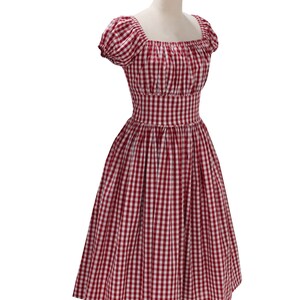 May include: A red and white gingham dress with a square neckline and short, puffed sleeves. The dress has a fitted bodice and a flared skirt, creating a classic, vintage silhouette. The fabric is a classic gingham pattern, perfect for a summer day.