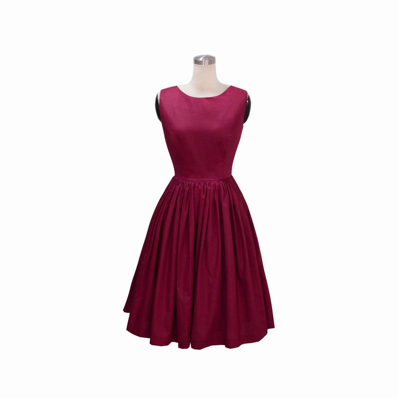 May include: A sleeveless, knee-length dress in a deep burgundy color. The garment features a round neckline, a fitted bodice, and a full, pleated skirt that flares out from the waistline. The fabric has a subtle sheen and a smooth texture.