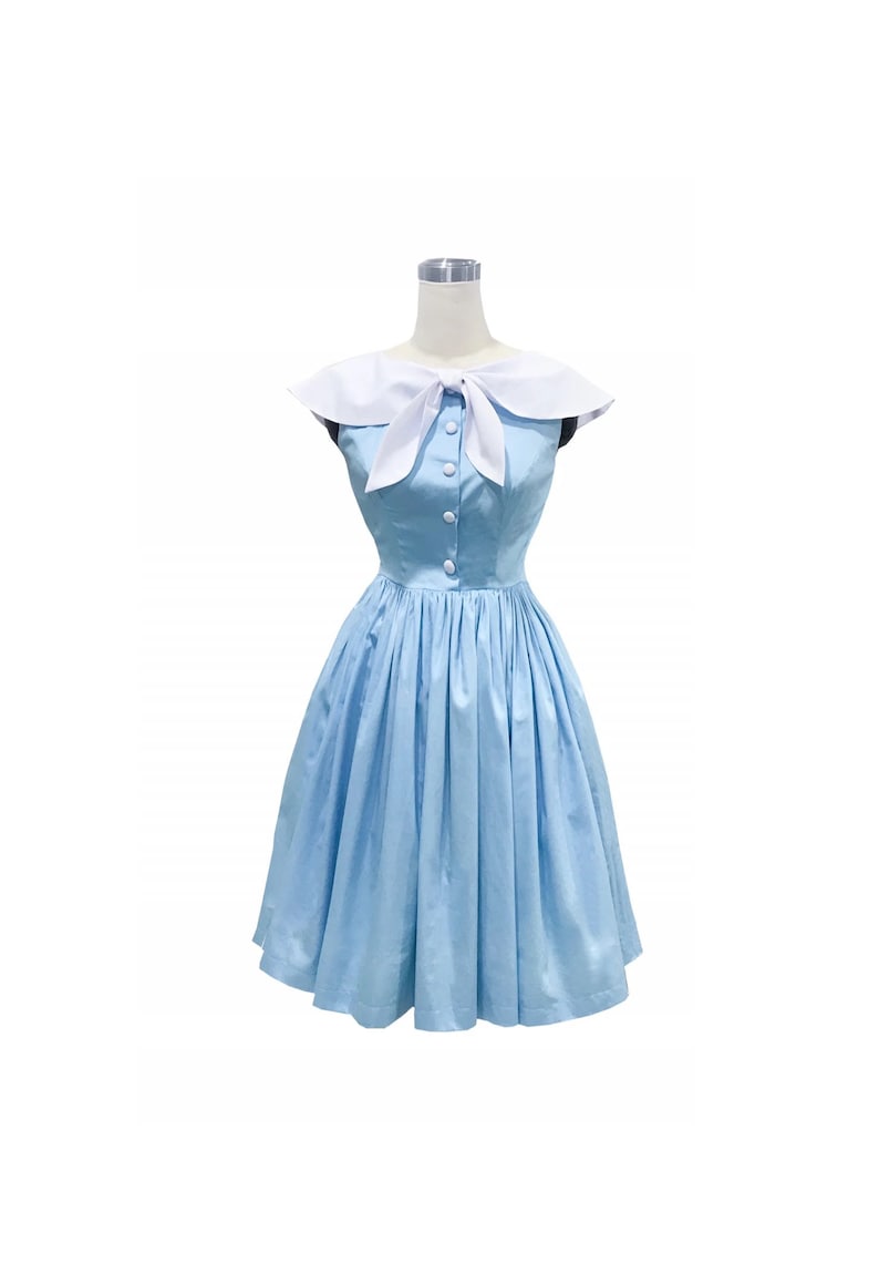 May include: A light blue sleeveless dress featuring a white sailor-style collar with a front tie detail. The bodice includes a vertical row of white buttons down the center, and the skirt is pleated, falling to a knee-length hemline.