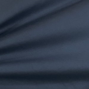 May include: A close-up of a dark blue fabric with a smooth texture. The fabric is folded and draped, creating soft folds and shadows.