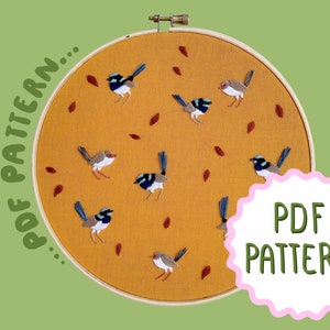 May include: A PDF pattern for embroidery featuring a design of blue and gray birds with brown leaves on a mustard yellow background. The pattern is displayed in a wooden embroidery hoop.