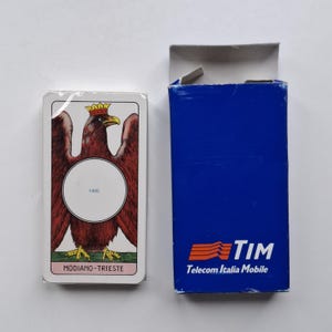 Può includere: Un mazzo di carte Modiano-Trieste confezionato, con un'aquila rossa coronata e un cerchio bianco. La scatola blu presenta il logo TIM Telecom Italia Mobile.