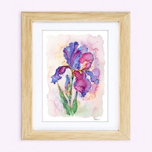 May include: A framed watercolor painting of a single iris flower with vibrant purple and magenta petals, green stems, and a soft, blended pastel background. The artwork is encased in a light-toned wooden frame with a white mat border.