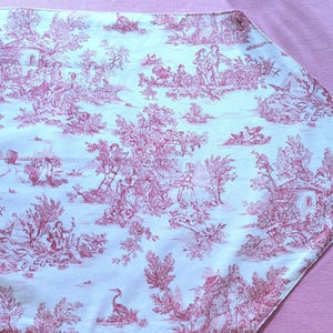 Peut inclure: Un chemin de table blanc avec un motif toile rose représentant un motif répétitif d'arbres, d'oiseaux et de personnes. Le motif est sur un fond blanc.