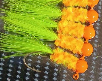 May include: A close-up of six fishing lures with bright orange and yellow fuzzy bodies and green and white feathers. The lures are attached to hooks.