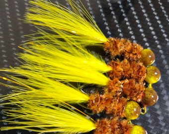 May include: A close-up of five yellow and brown fishing lures with a fuzzy texture. The lures have a round, shiny, gold-colored head.