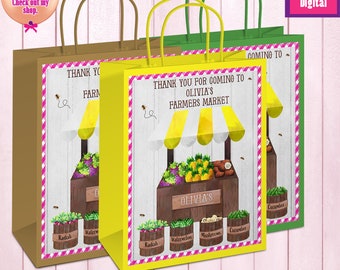 May include: Three colorful gift bags with handles. Each bag features a farmers market design with the text "Thank you for coming to Olivia's Farmers Market." The bags are brown, yellow, and green.