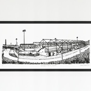 Peut inclure: Dessin au trait en noir et blanc d'un stade sportif, encadré en noir. L'œuvre représente l'extérieur d'un bâtiment avec des fenêtres et une structure métallique. Le stade est entouré d'herbe et possède plusieurs lampadaires.