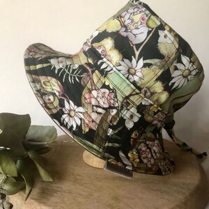 May include: A black and green sun hat with a floral print featuring small, colourful creatures. The hat has a wide brim and a tie string.