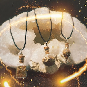 May include: Three gold-filled glass vials on black cords, each with a cork stopper, hanging from a white crystal geode. The vials are filled with gold flakes.