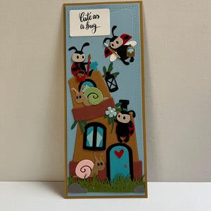 May include: A charming greeting card design with a house inhabited by ladybug characters. The card has a blue backdrop and a brown border. The text "Cute as a bug" is displayed on a white rectangle. Ladybugs are shown with different accessories.