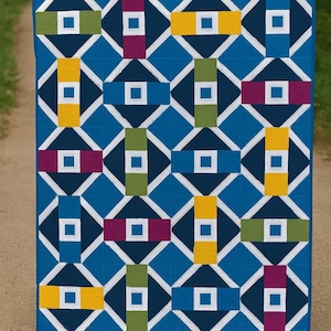 Puede incluir: Un edredón azul con un patrón geométrico. El diseño presenta diamantes blancos y rectángulos en amarillo, verde y morado. El edredón se exhibe al aire libre.