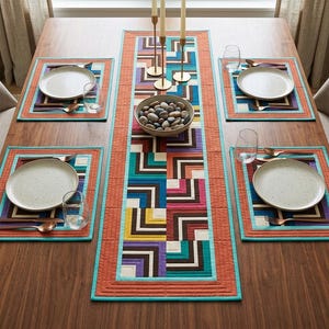 Op de afbeelding: Een houten eettafel gedekt voor een maaltijd, met een kleurrijke geometrisch patroon tafelloper en bijpassende placemats. Elke plaatsing bevat een wit bord, bestek en een waterglas. Een kom met stenen en kandelaars staan ook op de tafel.