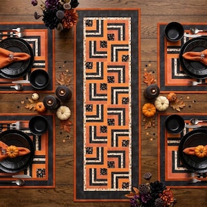 Op de afbeelding: Een feestelijke Halloween-tafelsetting met zwarte borden, oranje servetten en pompoenaccenten. De tafel heeft een patroonloper en placemats in zwart, oranje en wit. Inclusief bestek, kommen en decoratieve kaarsen.