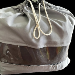 May include: A gray drawstring bag with a clear plastic window. The bag has a white drawstring and is made of a soft, fabric material.