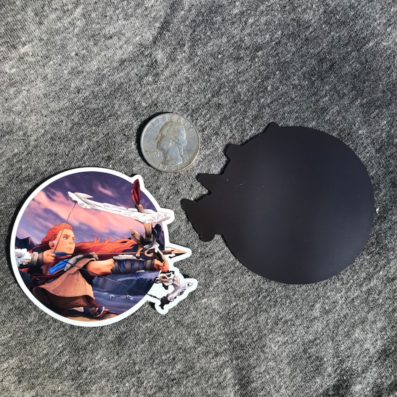May include: A round magnet featuring a colorful illustration of a woman with red hair holding a bow and arrow. The background is a purple and pink sunset. The magnet is approximately 3 inches in diameter.
