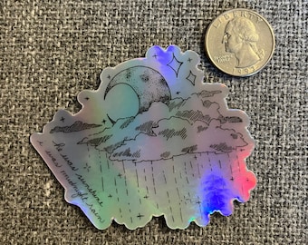 May include: Holographic sticker featuring a crescent moon, clouds, and rain, with the text "he was sunshine, i was midnight rain." The sticker has a black and white illustration style with a shimmering, iridescent finish. A US quarter is next to the sticker.