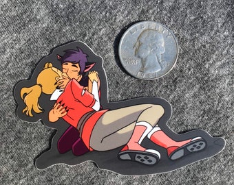May include: A sticker featuring a cartoon illustration of two characters embracing and kissing. One character has blonde hair and the other has purple hair. The sticker is on a gray surface next to a quarter.