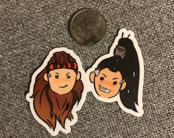 May include: Two cartoon character stickers, one with brown hair and a red and black headband, the other with black hair and a ponytail. Both characters have brown eyes and are smiling.