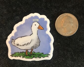 May include: A white duck with a halo above its head, standing on a patch of green grass. The duck is depicted against a blue background.