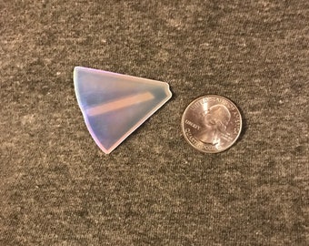 May include: A small, iridescent, triangular-shaped object with a light-colored stripe, next to a United States quarter. The object has a translucent appearance with hints of blue and purple. The quarter is silver in color.