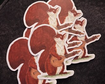 May include: A collection of stickers featuring a cartoon squirrel playing a ukulele. The squirrels have reddish-brown fur, white bellies, and are depicted with a cheerful expression. The stickers are on a white background.