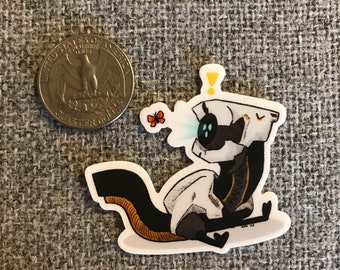 May include: A white and black robot with a yellow exclamation point above its head, sitting on a white background. The robot has a black tail and is looking at a small orange butterfly.