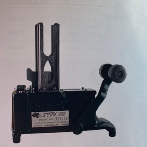 Peut inclure: Machine à équeuter en métal noir avec un levier et une poignée. La machine porte une étiquette indiquant "Steelpix Stemming Machine Model 150G Serial 152679".