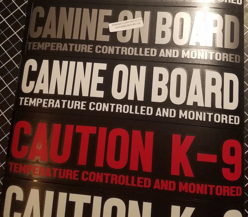 Op de afbeelding: Drie zwarte en zilveren reflecterende stickers met witte tekst die "CANINE ON BOARD TEMPERATURE CONTROLLED AND MONITORED" luidt. De derde sticker is rood en zwart en luidt "CAUTION K-9 TEMPERATURE CONTROLLED AND MONITORED".
