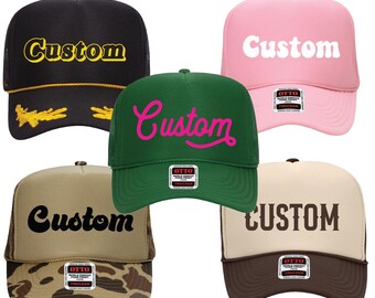 May include: Five trucker hats in various colors: black, pink, green, tan, and brown. Each hat features the word "Custom" in a different font and color. The hats have a mesh back and a curved brim.