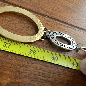 Puede incluir: Un cintur&oacute;n de metal dorado y plateado con eslabones ovalados y de cadena. El cintur&oacute;n se mide con una cinta m&eacute;trica amarilla, que muestra una longitud de aproximadamente 102 cm.