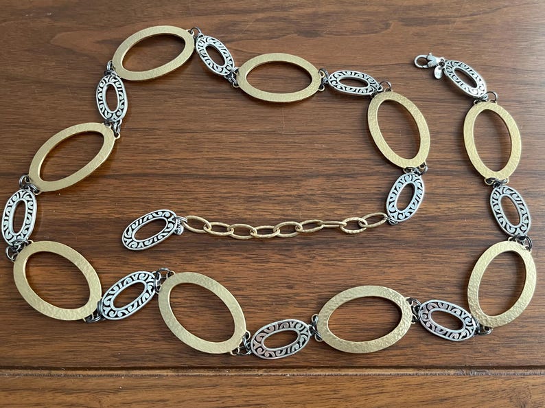 Puede incluir: Un collar dorado y plateado con eslabones ovalados. El collar presenta eslabones ovalados dorados y plateados alternos, conectados por eslabones de cadena dorados m&aacute;s peque&ntilde;os. El cierre es plateado.