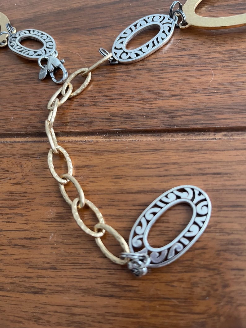 Puede incluir: Un cintur&oacute;n de metal plateado y dorado con eslabones ovalados. Los eslabones ovalados tienen un dise&ntilde;o decorativo de filigrana. El cintur&oacute;n tiene un cierre de mosquet&oacute;n y una cadena de eslabones ovalados dorados.