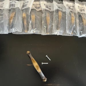 May include: Several antique brass cabinet handles, each in a clear plastic bag with screws. One handle and two screws are loose. The handles have a curved design with decorative ends.