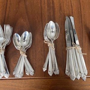 May include: A set of vintage silverware, including forks, spoons, and butter knives, all bundled together with twine. The silverware is made of polished silver and has a classic design.