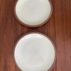 May include: Two ceramic plates with a light green glaze and a brown rim. The plates are on a wooden surface.