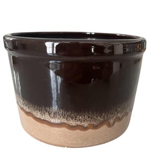 May include: A dark brown ceramic pot with a glossy finish. The bottom portion of the pot has a textured, light tan color. The pot is round with a wide opening, suitable for plants or storage.
