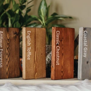 May include: A display of six rectangular wooden blocks, each with a different stain color. The colors are labeled: Vintage Greige, Antique Espresso, English Toffee, Classic Chestnut, Coastal Gray, and Rustic Pine. The blocks are arranged on a white surface.