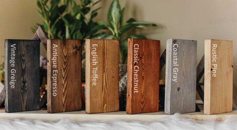 May include: A display of six rectangular wooden blocks, each with a different stain color. The colors are labeled: Vintage Greige, Antique Espresso, English Toffee, Classic Chestnut, Coastal Gray, and Rustic Pine. The blocks are arranged on a white surface.