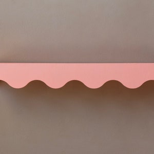 Peut inclure: Une &eacute;tag&egrave;re rose &agrave; bord festonn&eacute;. L'&eacute;tag&egrave;re est en bois et peinte d'une couleur rose clair.