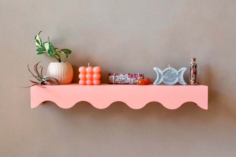 Peut inclure: Une &eacute;tag&egrave;re rose avec un bord festonn&eacute;, d&eacute;cor&eacute;e d'une plante en pot, d'une petite bougie orange, d'un bouquet de sauge, d'une bougie triple lune argent&eacute;e et d'une petite bouteille en verre remplie de fleurs s&eacute;ch&eacute;es.