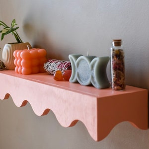 Peut inclure: Une &eacute;tag&egrave;re rose avec un bord festonn&eacute;, d&eacute;cor&eacute;e d'une plante en pot, de trois bougies, d'un bouquet de sauge et d'un petit bocal en verre rempli d'herbes s&eacute;ch&eacute;es.