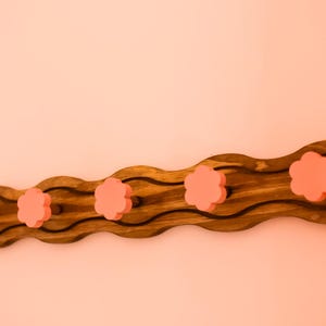 May include: A wooden coat rack with a wavy design and five pink flower-shaped knobs.