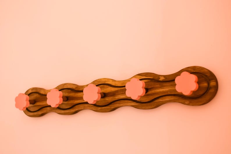 May include: A wooden coat rack with a wavy design and five pink flower-shaped knobs.