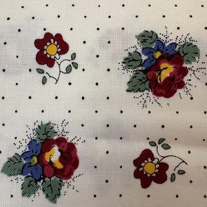 May include: A white fabric featuring a repeating pattern of small black polka dots. The design includes clusters of red and blue flowers with yellow centers and green leaves, interspersed with smaller individual red flowers with yellow centers.