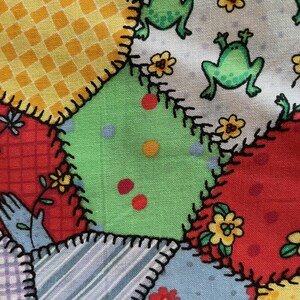 May include: A patchwork fabric with a variety of colorful patterns, including yellow and red plaid, green with red dots, and white with green frogs. The fabric is sewn together with black stitching.